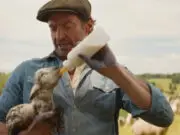 Hugh Jackman feeds a lamb milk from a bottle in the 2026 film, The Sheep Detectives.