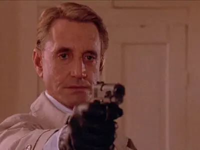 Roy Scheider points a pistol at someone off screen while wearing a black glove in the film, Cohen & Tate.