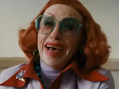 Amy Madigan with fiery red hair, blue-tinged large spectacles and overdone red lipstick in the horror film Weapons.