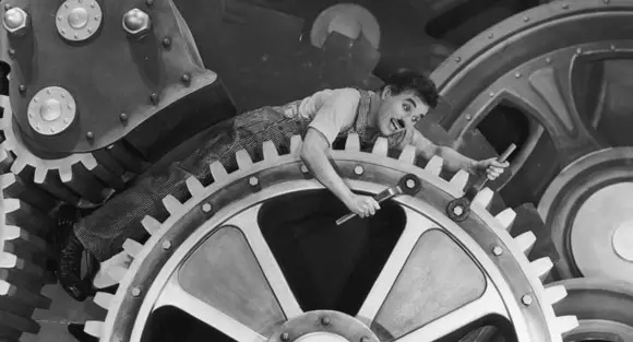 Charlie Chaplin in one of the most famous silent film black and white scenes, as he makes his way through the large cogs of a giant industrial machine.