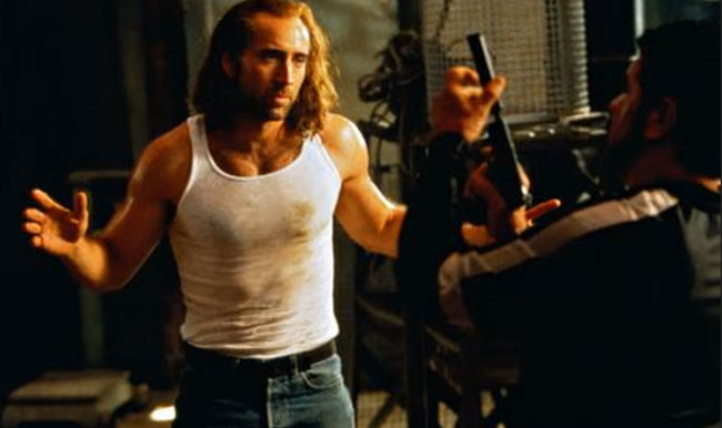 Nicolas Cage holds his hands up while wearing a white vest top in the film Con Air.