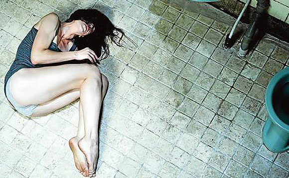 Charlotte Gainsbourg lies on a hard floor looking upset with bare feet in Lars von Trier's Antichrist.
