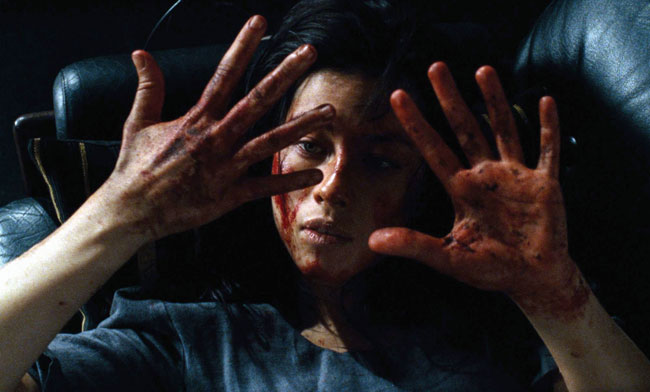A bloodied young woman stares at the camera with her hands held up, her fingers showing signs of torture.